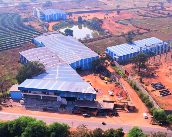 Aerial view of the Gurunanak Agriculture plant: blue-roofed production halls beside a road, with fields around them